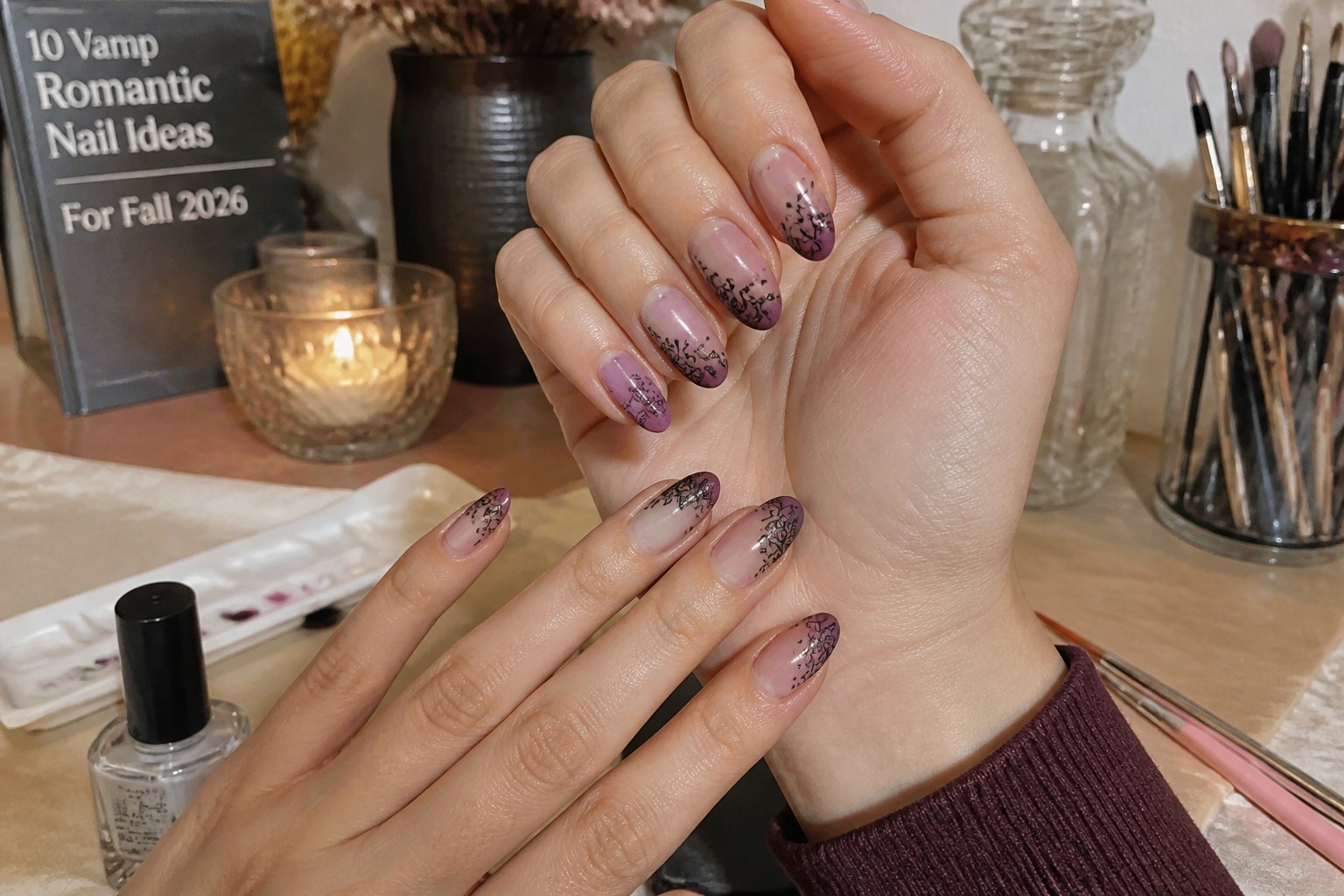 Close-up of hands with rose-bluish ombre nails featuring black lace details, surrounded by nail art tools on a warm fall background.